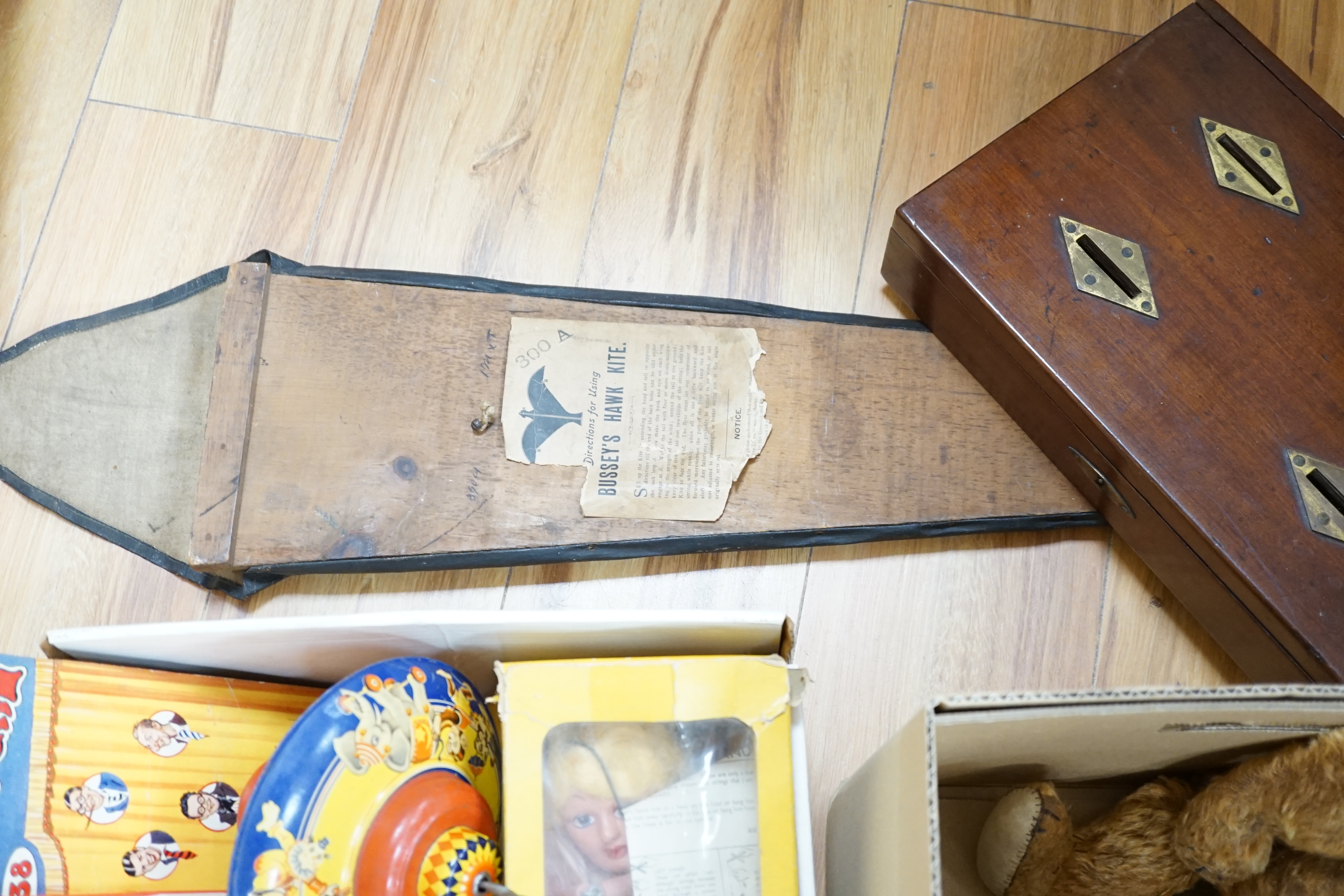 An early 20th century cased Bussey’s Hawk kite, a black walkie talkie doll, a four slot money box, an early Pelham puppet and two others, a hump backed teddy, together with various games and soft toys